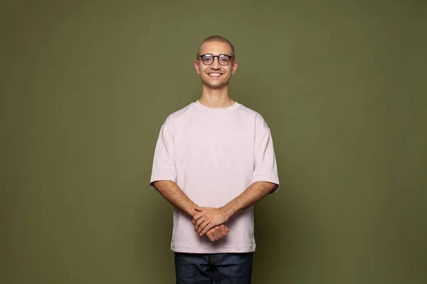 Happy creative man wearing t-shirt and glasses smiling standing on khaki green studio wall banner background