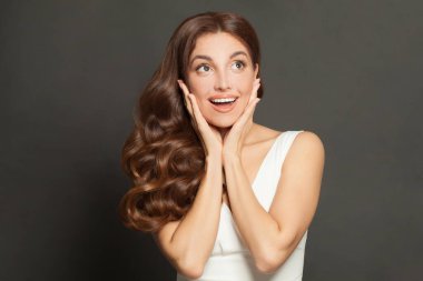 Neşeli, heyecanlı, şaşırmış, doğal makyajlı, kıvırcık, sağlıklı saçlı, gri arkaplanlı bir kadın.