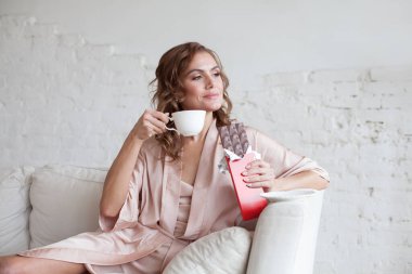 Woman eating chocolate. Beautiful young woman sitting on the coach and eating chocolate