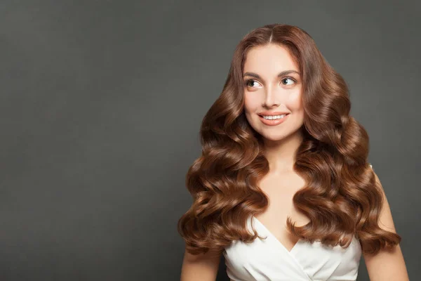 Happy model smiling. Healthy woman with long brown curly hairstyle on black
