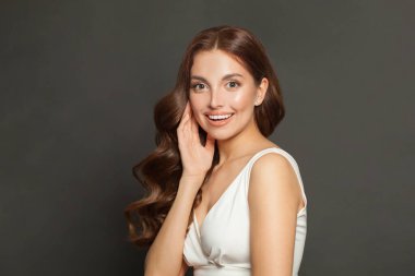 Pretty surprised woman with perfect clean skin, natural makeup and long healthy brown curly hair on gray studio background