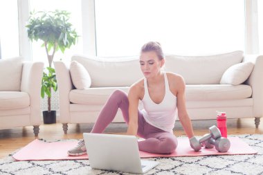 Cute woman doing exercise and watching online tutorials on laptop, training in living room