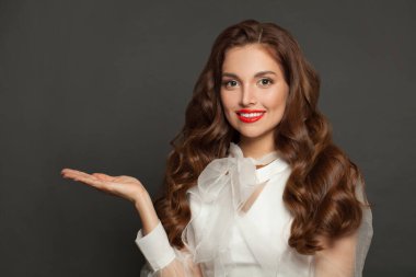 Cute perfect woman holding empty open hand and smiling on gray studio wall banner background