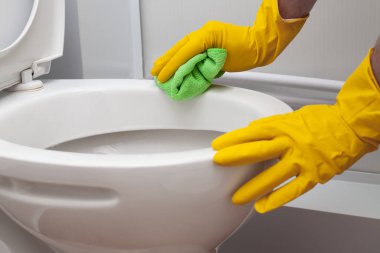 Man in yellow rubber gloves cleaning toilet with green cloth