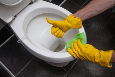 Man in rubber protective gloves cleaning and washing toilet and showing thumb up