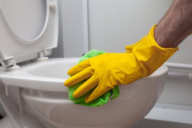 Man cleans a bathroom toilet with a green brush
