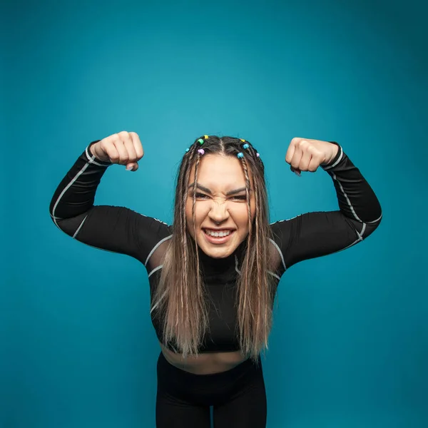 Emotional happy funny woman fitness winner showing her power on blue background
