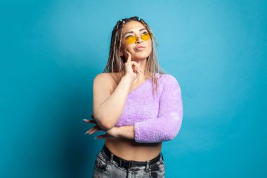 Düşünceli, çekici genç bir kadın mavi arka planda düşünüyor ve başka tarafa bakıyor.