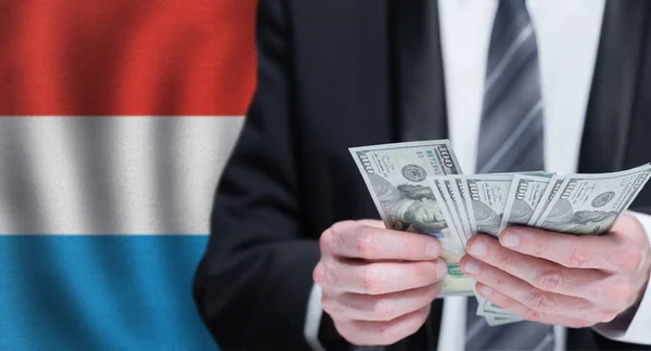 Hands holding dollar money on flag of the Grand Duchy of Luxembourg