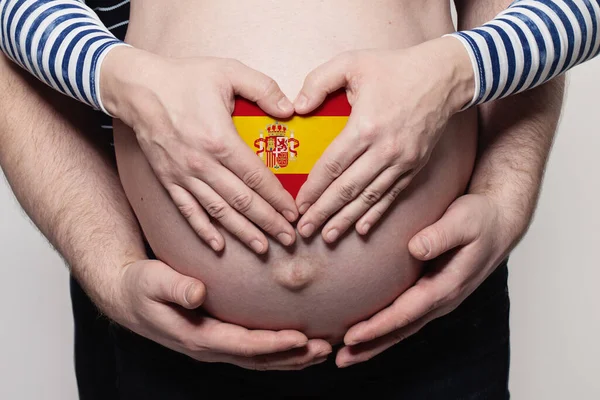 Spanish family concept. Man embracing pregnant woman belly and heart with flag of Spain colors closeup