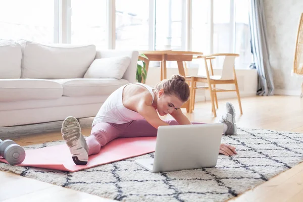 Young pretty woman exercising at home in a living room. Video lesson. Sportswoman repeating exercises while watching online workout session. Beautiful young woman doing fitness exercise at home