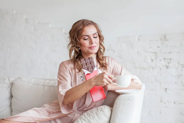 白い背景にソファに座っている間にチョコレートを食べるかなり若い女性の肖像画 — ストック写真