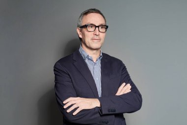 Portrait Of Mature Businessman in Suit Standing With Crossed Arms on Grey Background