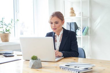 Modern ofisteki iş yerinde dizüstü bilgisayarla çalışan kendine güvenen bir iş kadını.