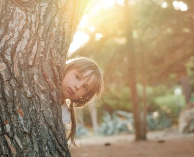 Ağacın arkasında durup dışarıdaki fotoğrafa bakan komik küçük kız.