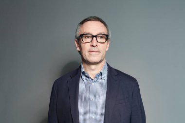 Gri arka planda gözlüklü 60 yaşındaki bir adamın portresi.