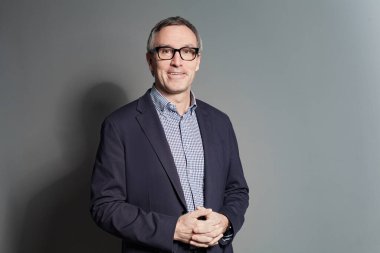 Confident businessman in formalwear looking at camera while standing against grey studio wall background