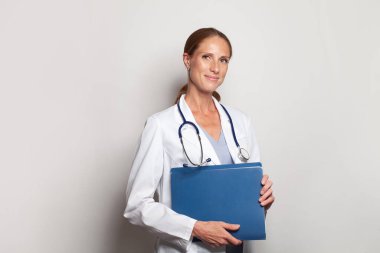 Cheerful young female doctor with stethoscope over neck looking at camera and smiling on white background
