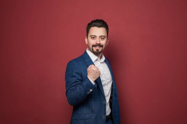 Kırmızı arka planda gülümseyen mavi takım elbiseli, kendinden emin, mutlu iş adamı.