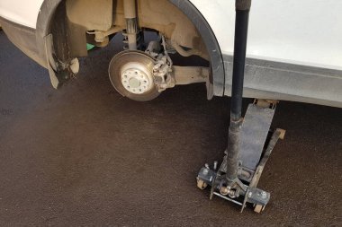 Closeup of a car lifted on jack in process of new wheel tire replacement. Breakdown of a vehicle on a road.