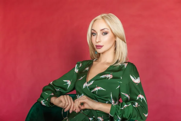 Fashion portrait of a smiling woman in a green dress on red