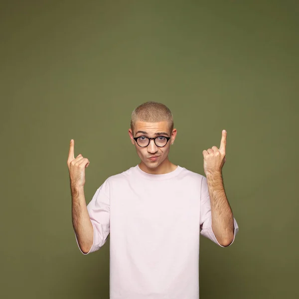 Portrait of cute guy in glasses pointing up at copy space on green background