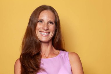 Attractive middle age woman with long brown hair and perfect smile on yellow background