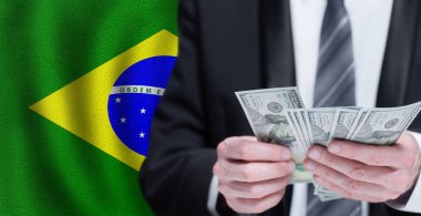 Hands holding dollar money on flag of Brazil