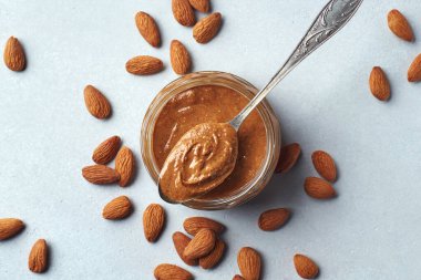 Açık gri arkaplanda cam kavanoz ve kaşık badem ezmesi, üst manzara, yukarıda.