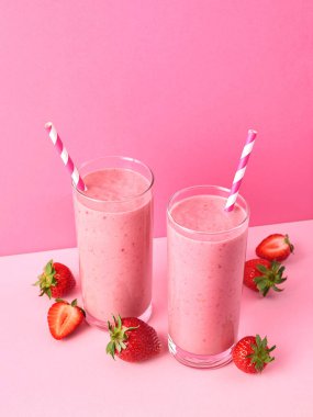 İki bardak çilekli smoothie veya pembe pastel arka planda milkshake, metin için fotokopi alanı. Sağlıklı kahvaltı içeceği.