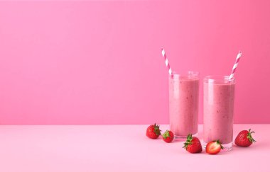 İki bardak çilekli smoothie veya pembe pastel arka planda milkshake, metin için fotokopi alanı. Sağlıklı kahvaltı içeceği.