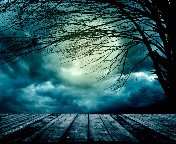 Old grunge wooden table in front of scary night scene. Halloween composition background with scary dark forest and evil moon. Mystery horror landscape.