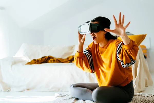 Excited casual clothing woman wearing virtual reality VR glasses headset in living room. Future trend using virtual reality goggles device for videogame and home entertainment. Futuristic technology experience.