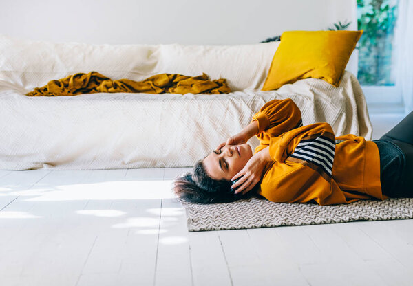 Woman in casual clothing with headphones lying down the floor in her living room and enjoys listening the music. Leisure time of single woman relaxing in isolation streaming songs from player. 