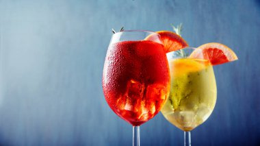 Tow glasses of red and yellow aperol spritz cocktail with rosemary and grapefruit on blue background. Summer party happy hour restaurant bar menu. Italian luxury garnish liquor aperitif  with sparkling soda and wine.