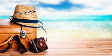 Vintage suitcase, sunglasses and hipster hat wooden deck and blur tropic sea background. Summer paradise cruise travel design layout banner. Tourism, beach, vacation travel destination concept wallpaper mockup.