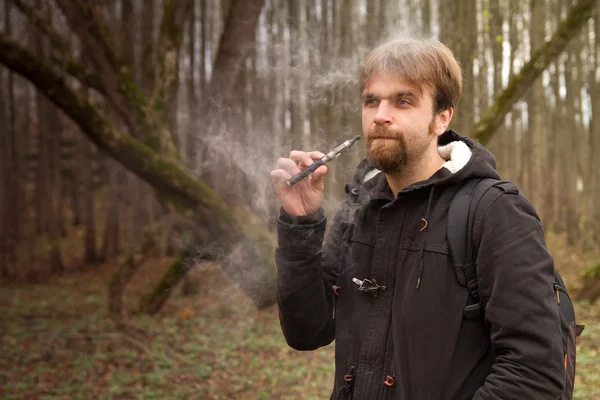 Man with the electronic cigarette in the park autumn — Stock Photo, Image