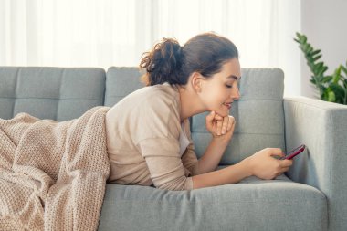 Mutlu, sıradan, güzel bir kadın evdeki kanepede oturan bir telefonu kullanıyor..