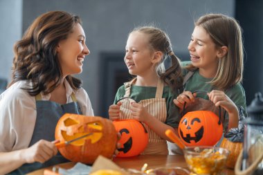 Mutlu Cadılar Bayramı! Anne ve kızları balkabağı oyuyor. Aile tatili için hazırlanıyor.