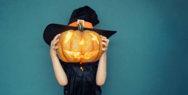 Mutlu Cadılar Bayramı! Mavi duvar arkasında cadı kostümü giymiş sevimli, gülen bir kız.. 