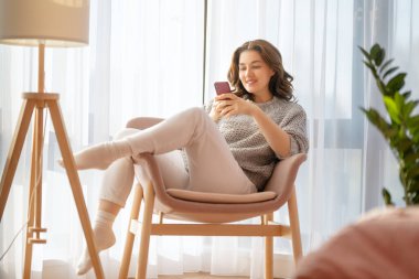 Mutlu, sıradan, güzel bir kadın telefonuyla evdeki koltukta oturuyor..