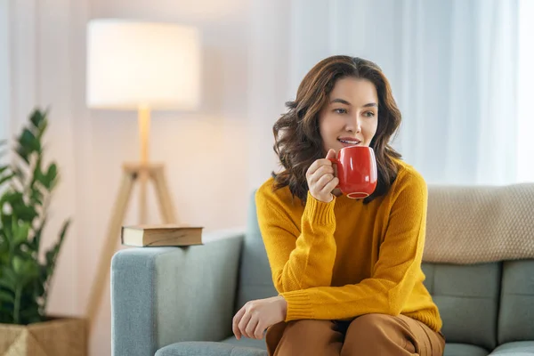 Beautiful young woman enjoying tea sitting on the sofa at home.