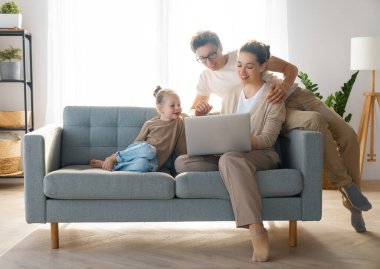 Sevgi dolu bir aile. Genç anne, baba ve kızı dizüstü bilgisayar kullanıyor. Komik anne, baba ve güzel çocuk evde kalarak eğleniyorlar..