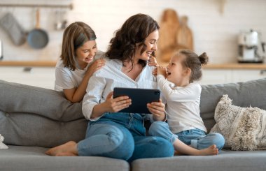 Sevgi dolu bir aile. Genç anne ve kızları arkadaşlarıyla uzaktan konuşmak için tablet bilgisayar kullanıyorlar. Komik anne ve güzel çocuklar evde kalarak eğleniyorlar..