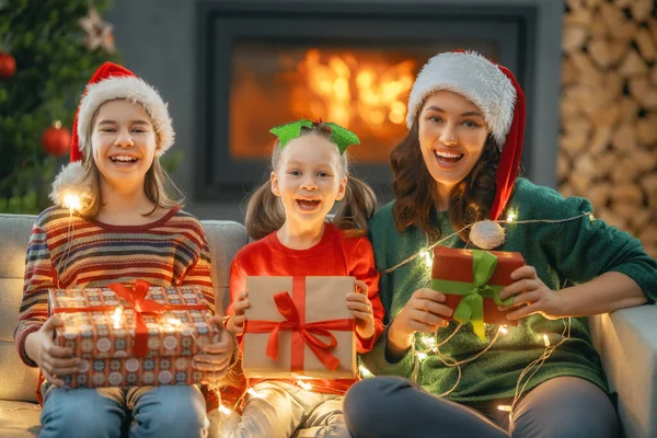メリークリスマスとハッピーホリデー 陽気な母親とかわいい娘たちが贈り物を交換します 屋内で木の近くで遊んでいるお母さんと小さな子供たち プレゼント付きの家族を愛する — ストック写真