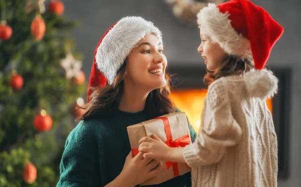 メリークリスマスとハッピーホリデー 陽気な母親とかわいい娘の女の子は贈り物を交換します 屋内で木の近くで遊んでいるお母さんと小さな子供 プレゼント付きの家族を愛する — ストック写真