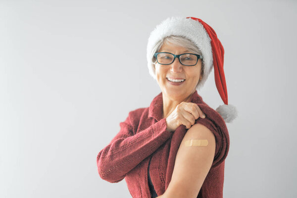 Старшая женщина после прививки в шляпе Санты. Защита от вирусов на рождественские праздники. COVID-2019.