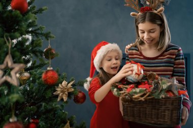 Mutlu Noeller ve mutlu tatiller. Evdeki neşeli, sevimli, çocuksu kızlar. Çocuklar sabah ağaçların yanında eğleniyorlar.