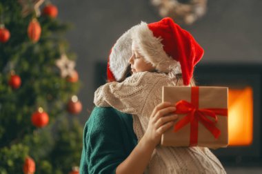 Mutlu Noeller ve mutlu tatiller. Neşeli anne ve tatlı kızı hediye değiş tokuşu yapıyor. Anne ve küçük çocuk içeride ağaçların yanında eğleniyorlar. Odasında hediyeler olan sevgi dolu bir aile.