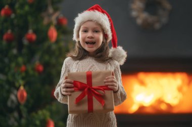 Mutlu Noeller ve mutlu tatiller! Hediyesi olan neşeli, sevimli bir kız çocuğu. Çocuk ağacın yanında eğleniyor..